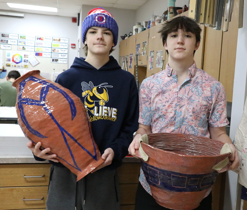 Two high school males hold giant pots they made in art class. 