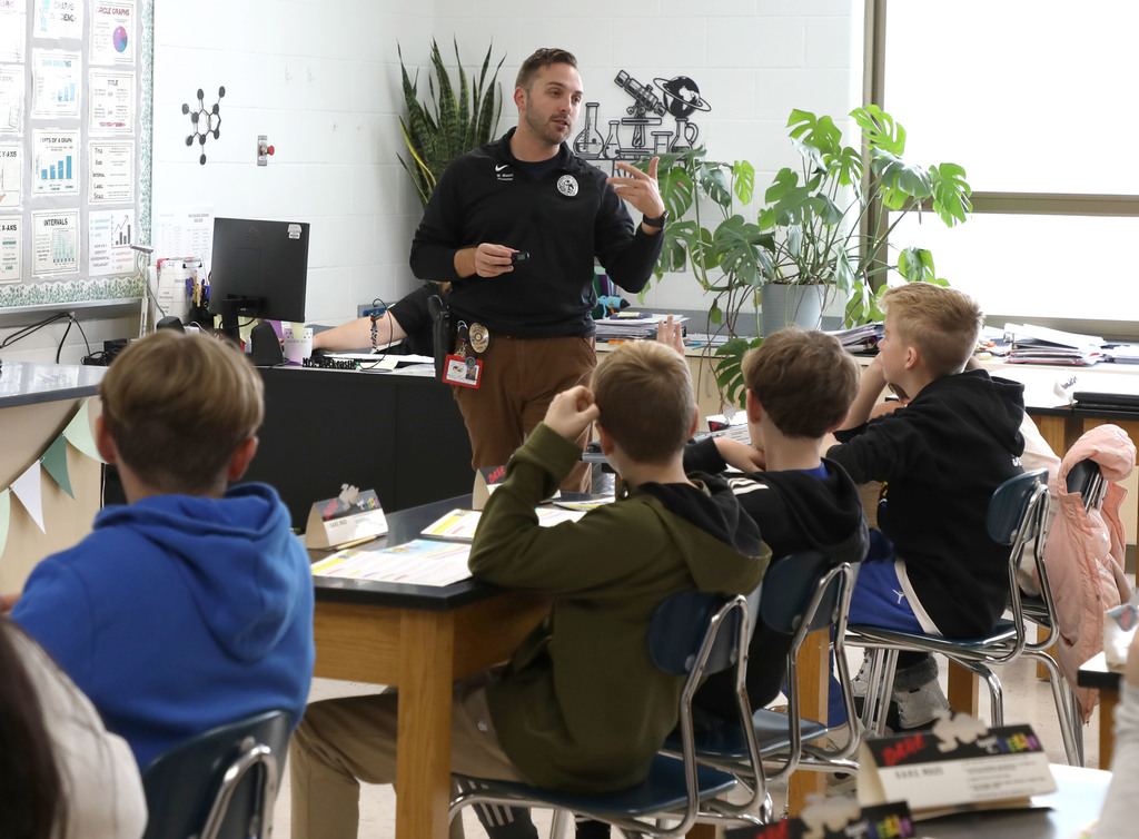 An adult male speaking to four jr. high boys in a classroom. 