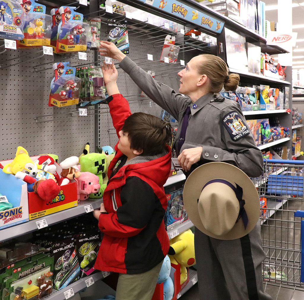 A female state trooper helps a boy get a toy off a store shelf. 