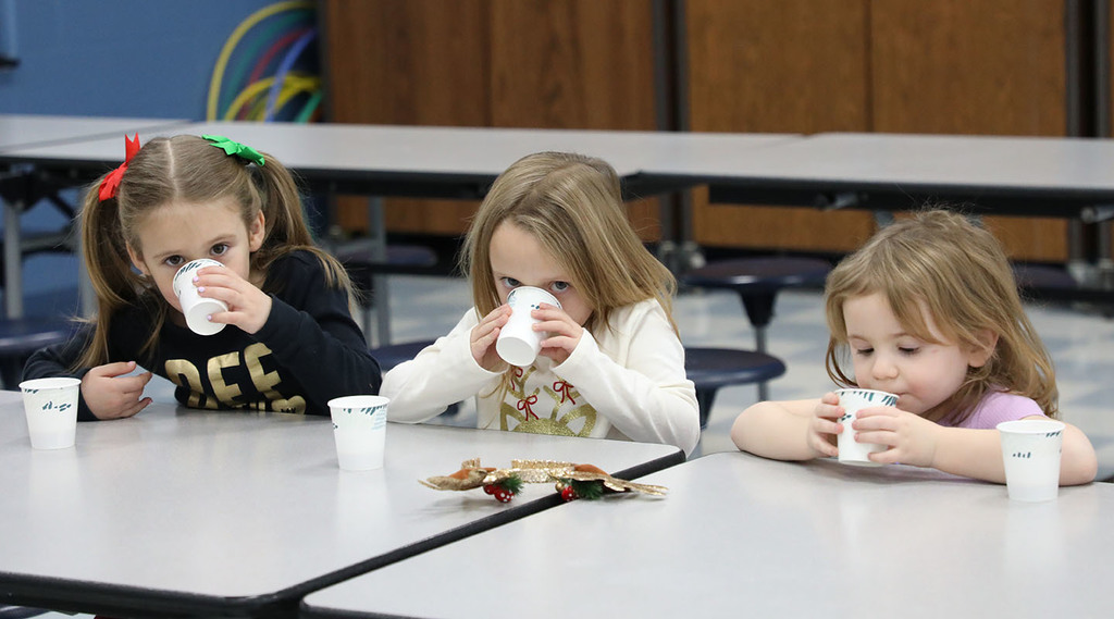 Three elementary girls are drinking out of cups. 