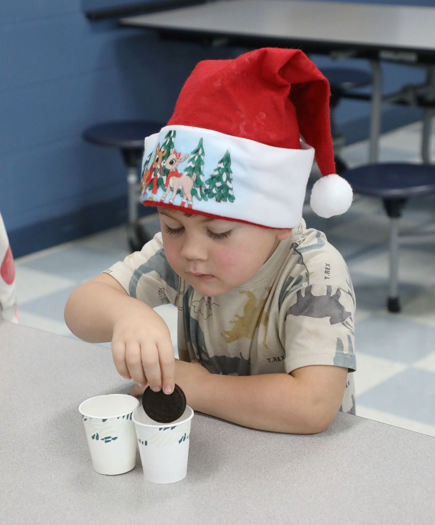 An elementary boy is dunking a cooking in a cup. He is wearing a Santa hat. 