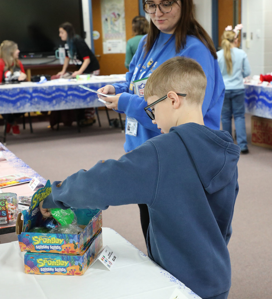 A male elementary student plays with a toy as a adult looks on. 