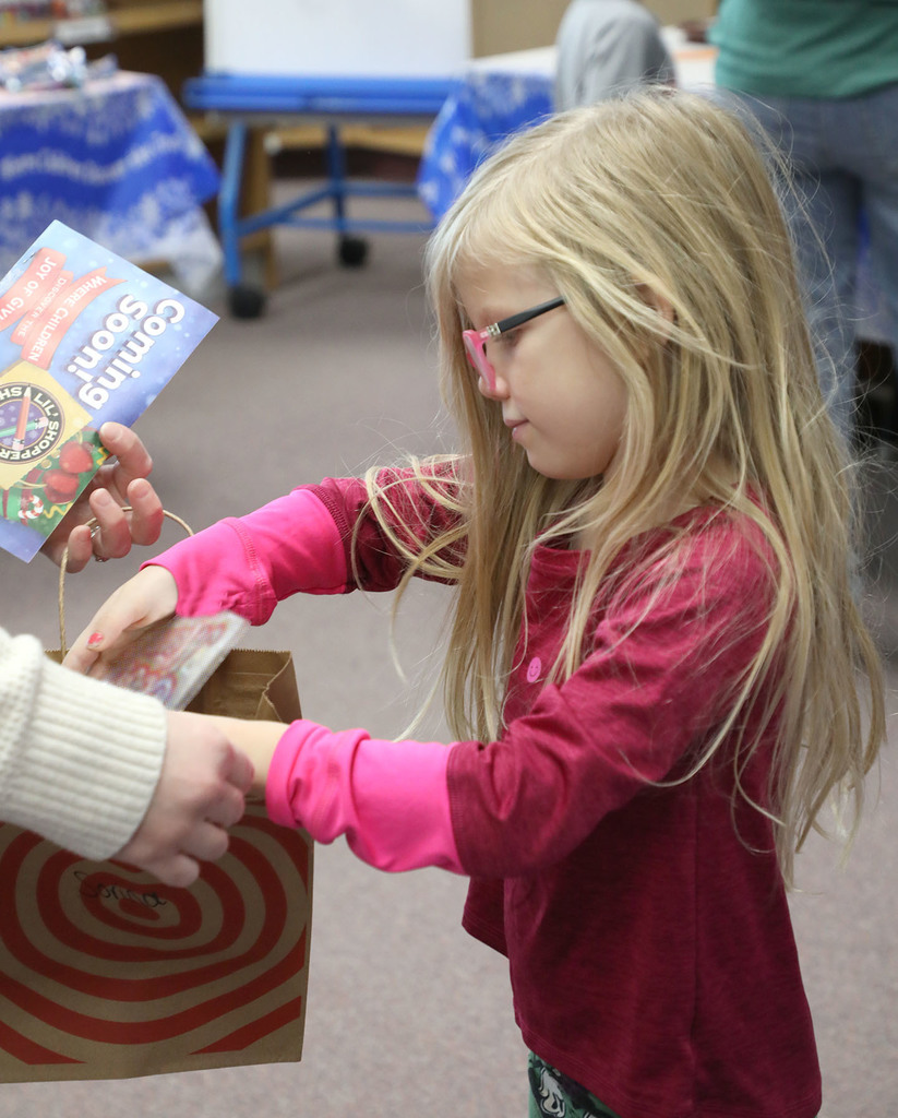 A female elementary student puts a gift in a paper bag. An adult is helping her but you cannot see the person. 