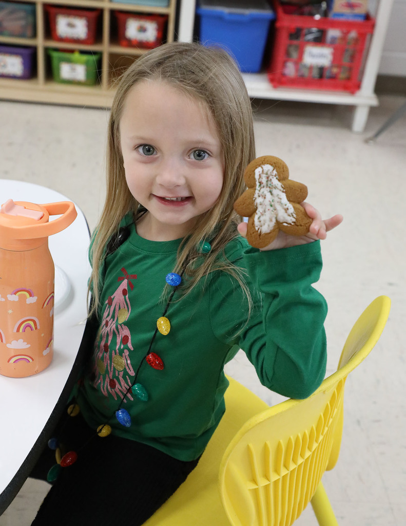 A girl elementary student holding up a gingerbread cookie. 