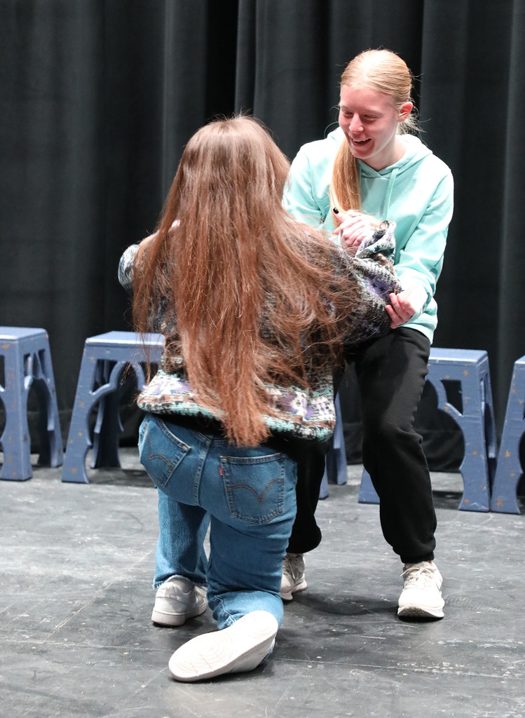 A teenage girl helping another teenage girl off the floor. 