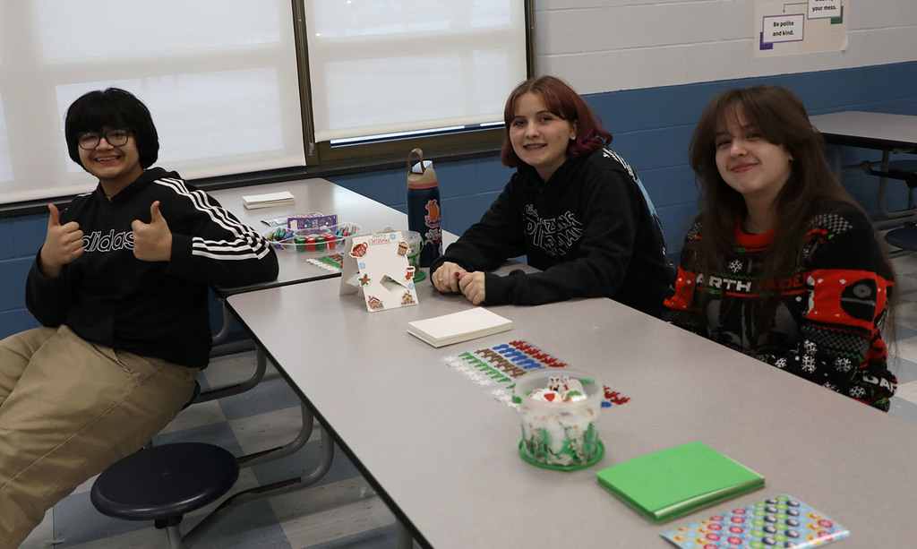 One male student with "thumbs up" sitting with two female students. 