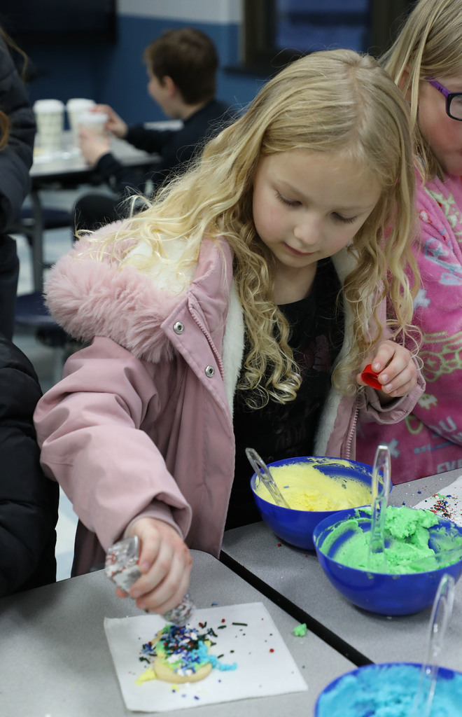 A female elementary student decorating holiday cookies. 