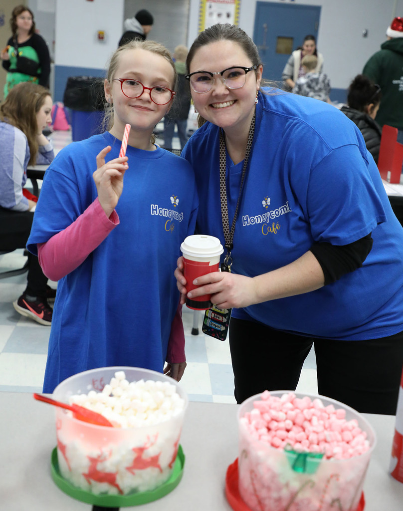 A female teacher smiling with a female student. One is holding a cup and the other is holding a candy cane. 