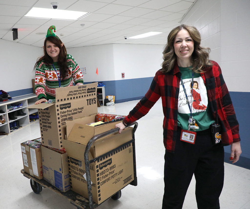 One female rolling a cart with boxes on it. Another female stands on the cart.