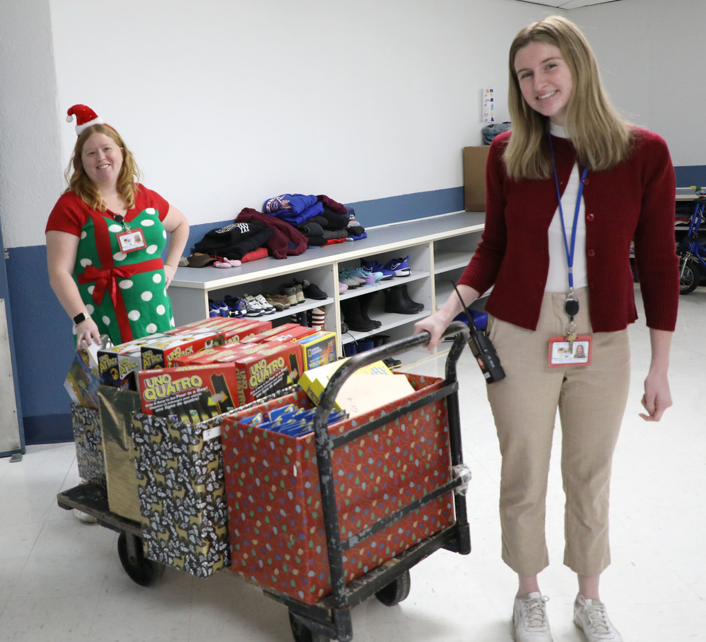 Two females rolling a cart with toys on it. 