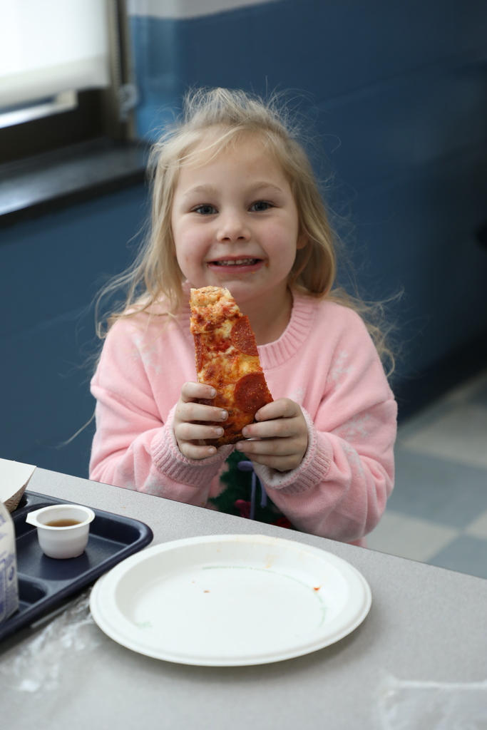 An elementary girl eating a piece of pizza. 