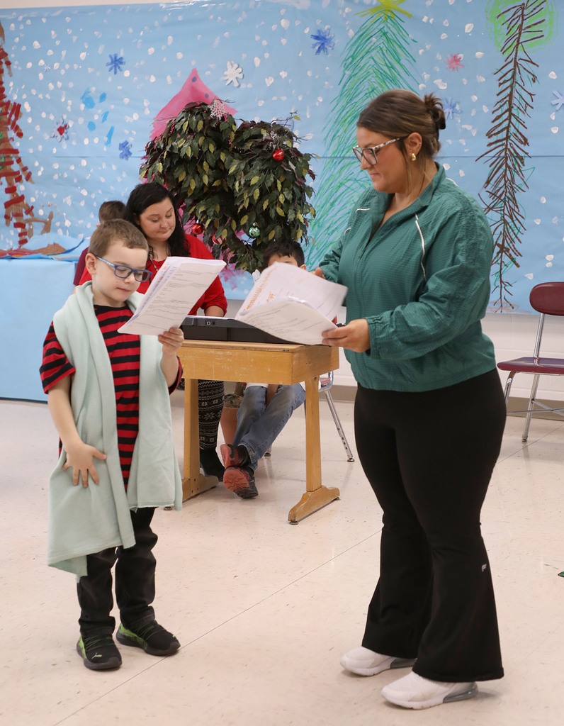 A female teacher and a male student standing together reading scripts. 