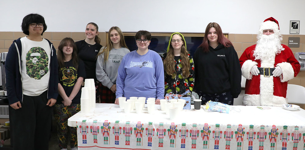 A group of high school students standing in front of a table with cups on it. Santa is standing with them. 
