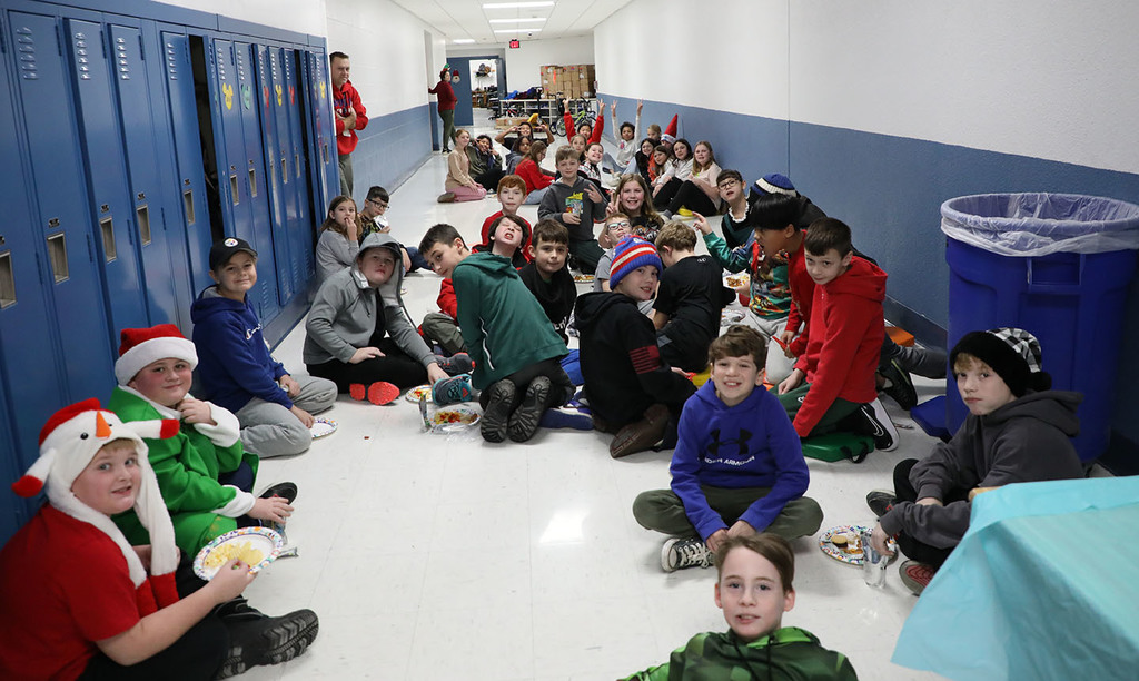A group of students sitting in a school hallway. Many are eating snacks. 