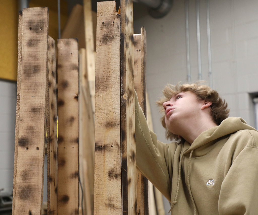 A high school boy working on a wood shelf that he is building. 