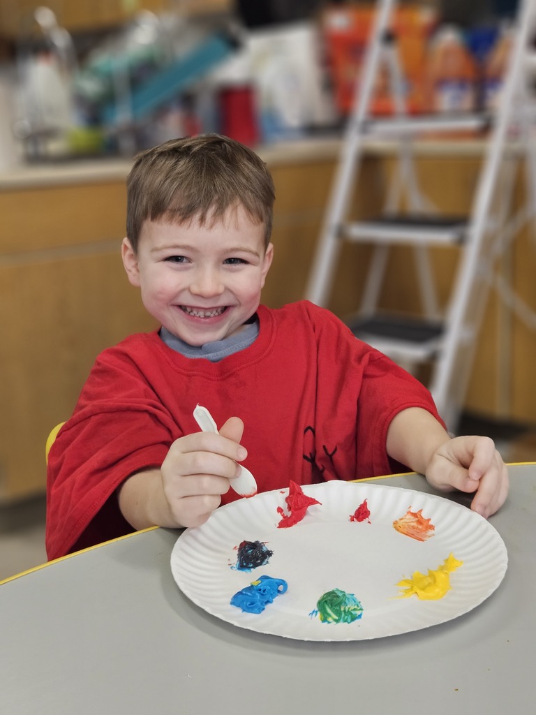 An elementary boy with a plate in front of him that has colored frosting on it. 