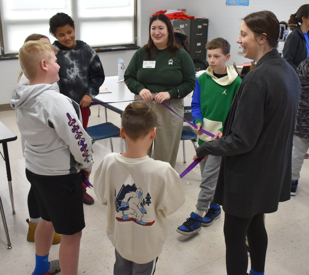 A group of elementary students and two adults holding onto a rope in a circle. 