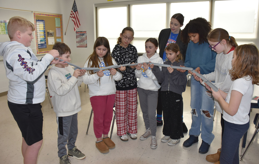 A group of elementary students and one teacher. The students are holding marble tubes. 