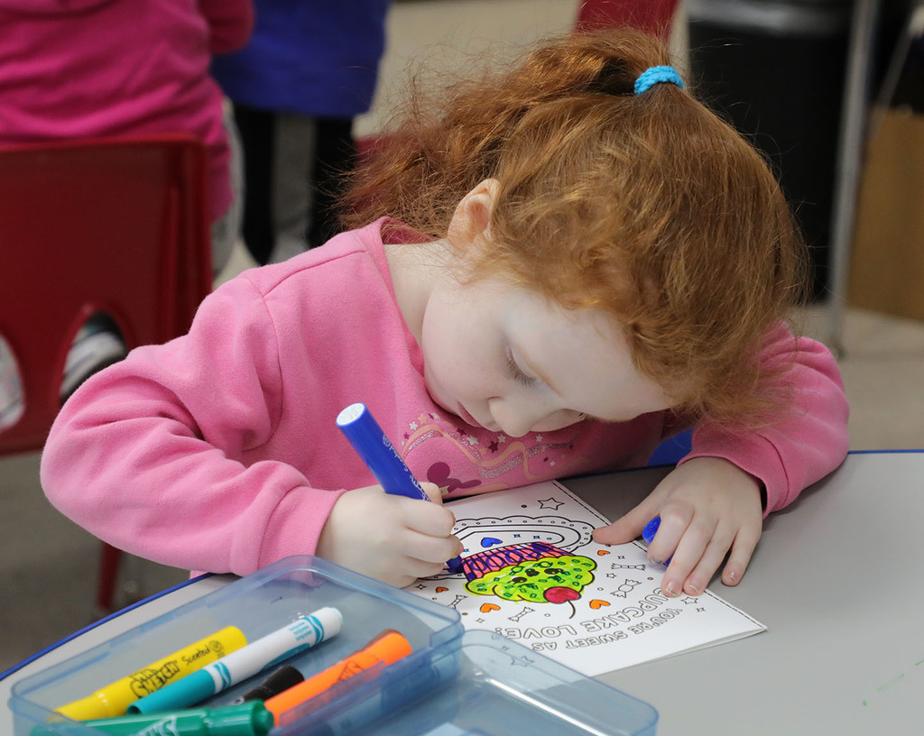 An elementary girl coloring a Valentine's Day card.