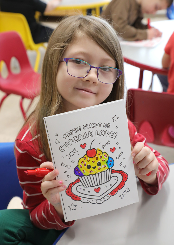 An elementary girl holding up a Valentine's Day card. 