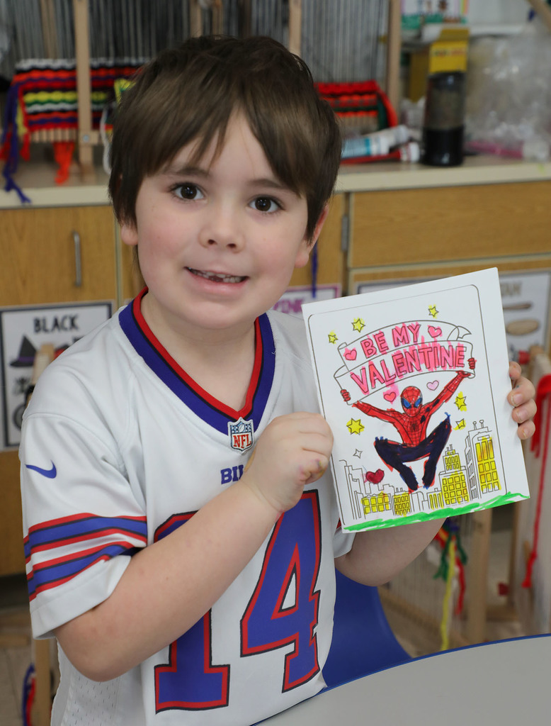 An elementary boy holding up a Valentine's Day card. 