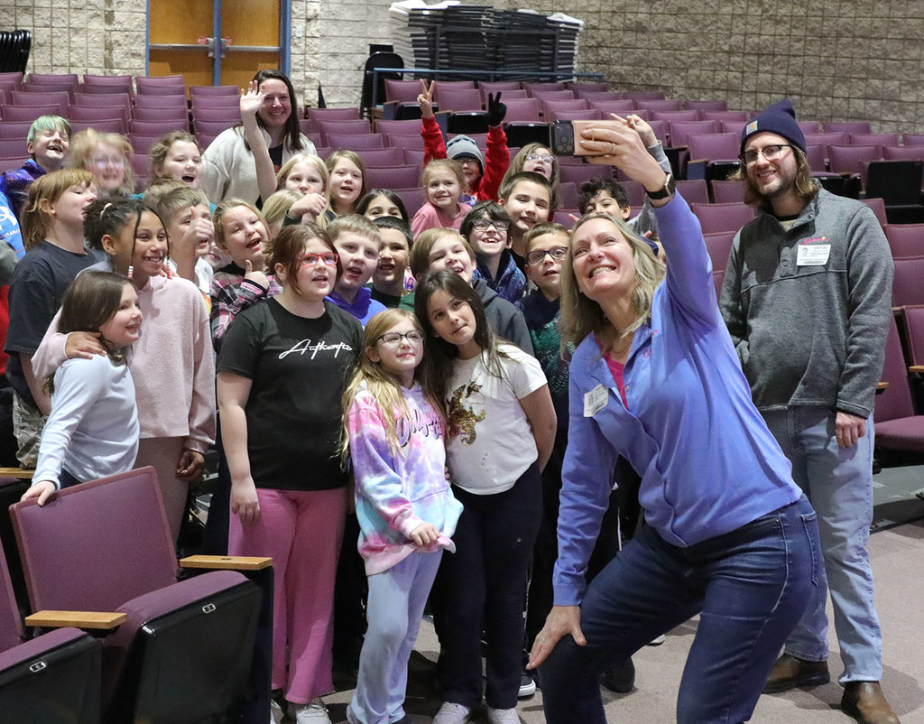 An adult taking a cell phone selfie with a group of 3rd graders. 