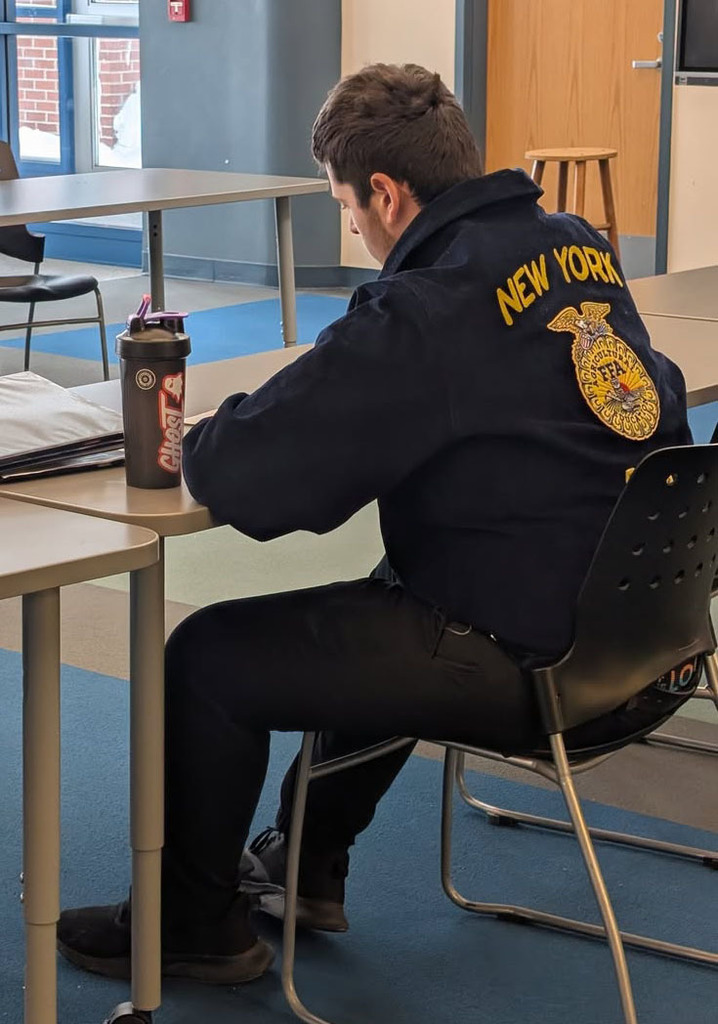 A boy sitting at a desk with an FFA jacket on. 