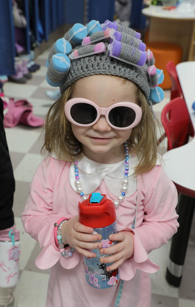 An elementary girl wearing a hat with hair rollers and sunglasses. 