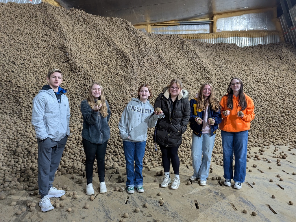 A group of high school students standing in front of a pile of potatoes. 