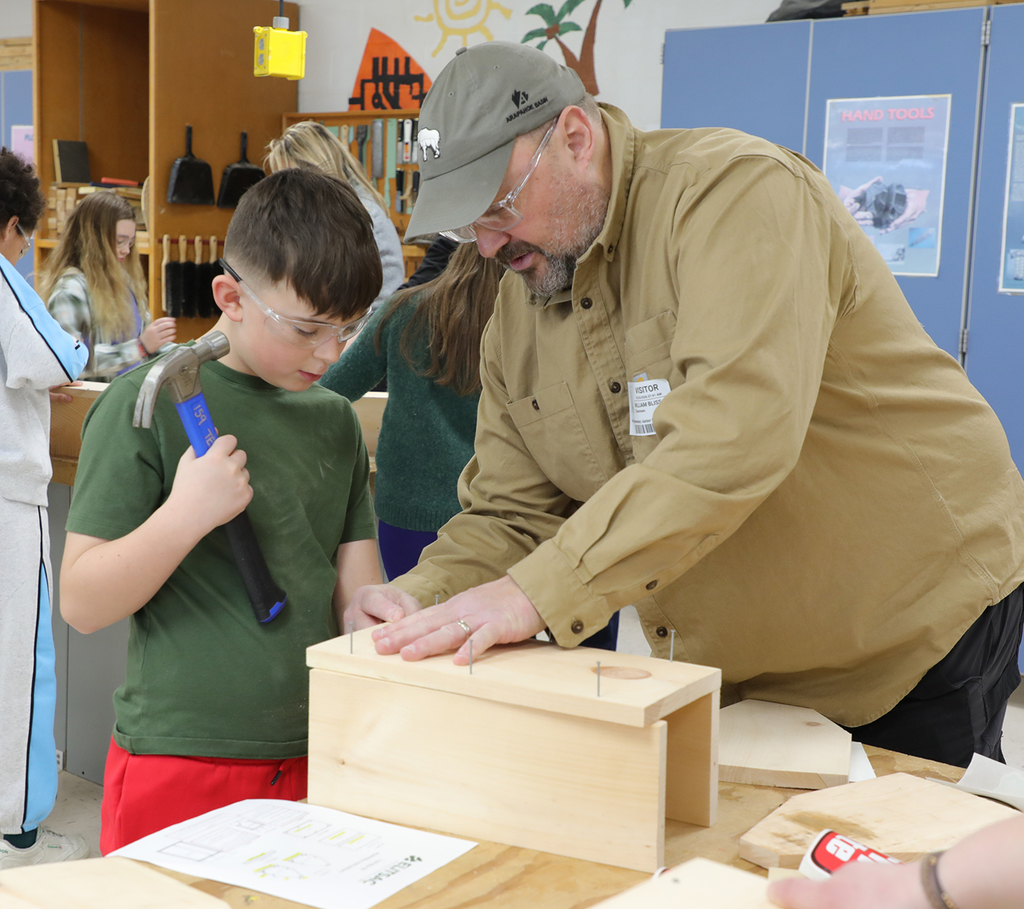 An adult male helping a 5th grade boy build a toolbox. 