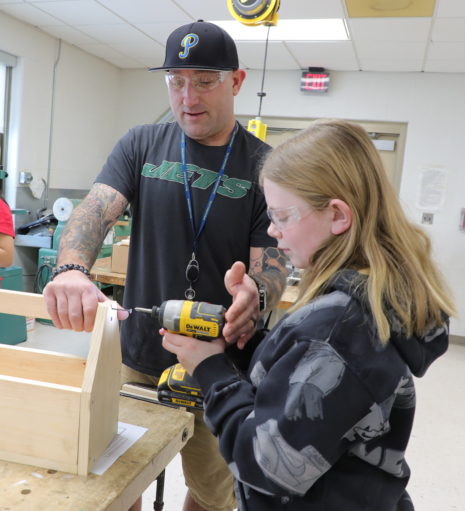 An adult male helping a 5th grade girl use a drill. 