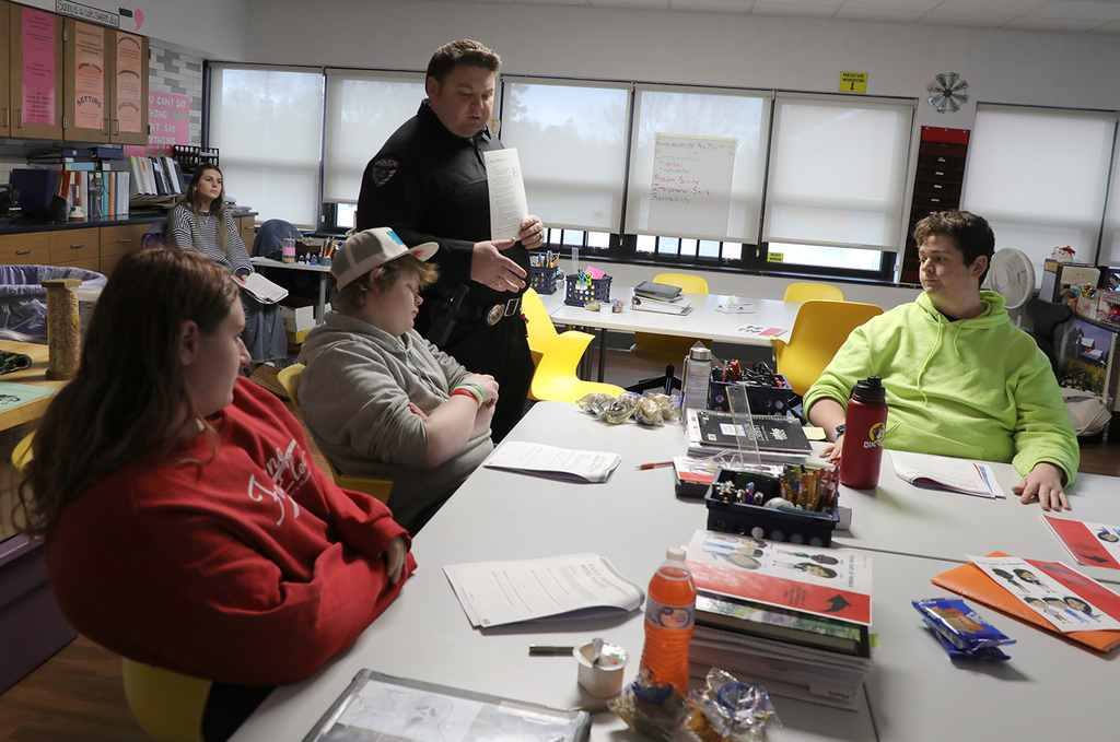 A police officer standing in a classroom talking to high school students. 