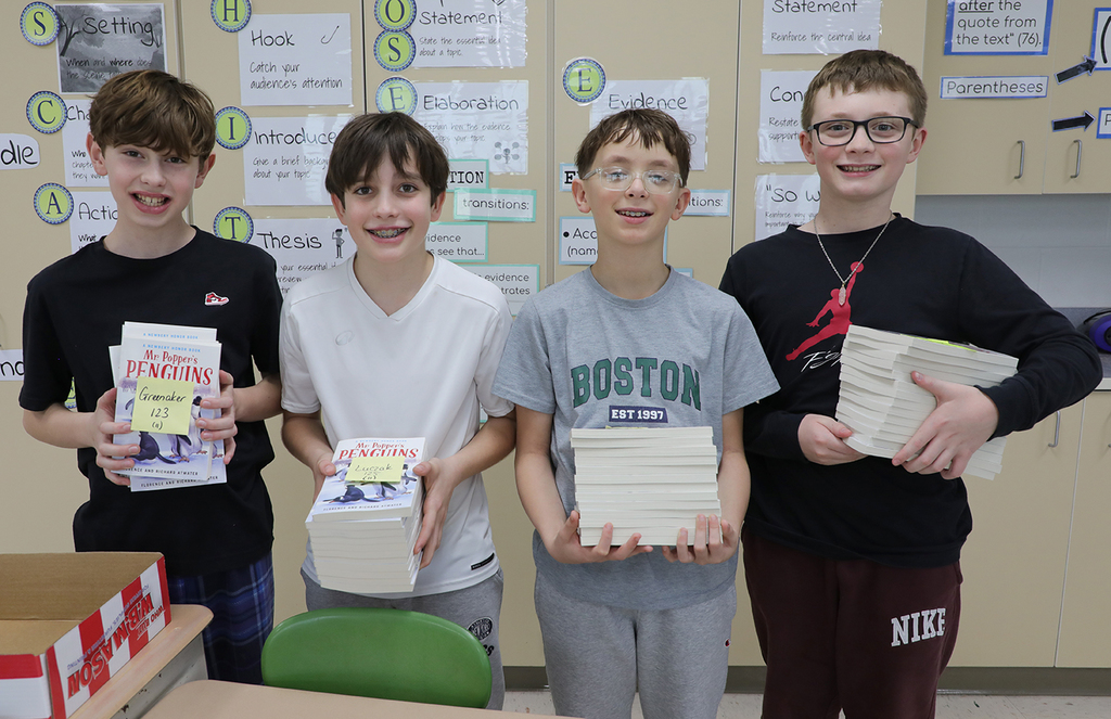 Four 6th grade boys holding piles of books. 