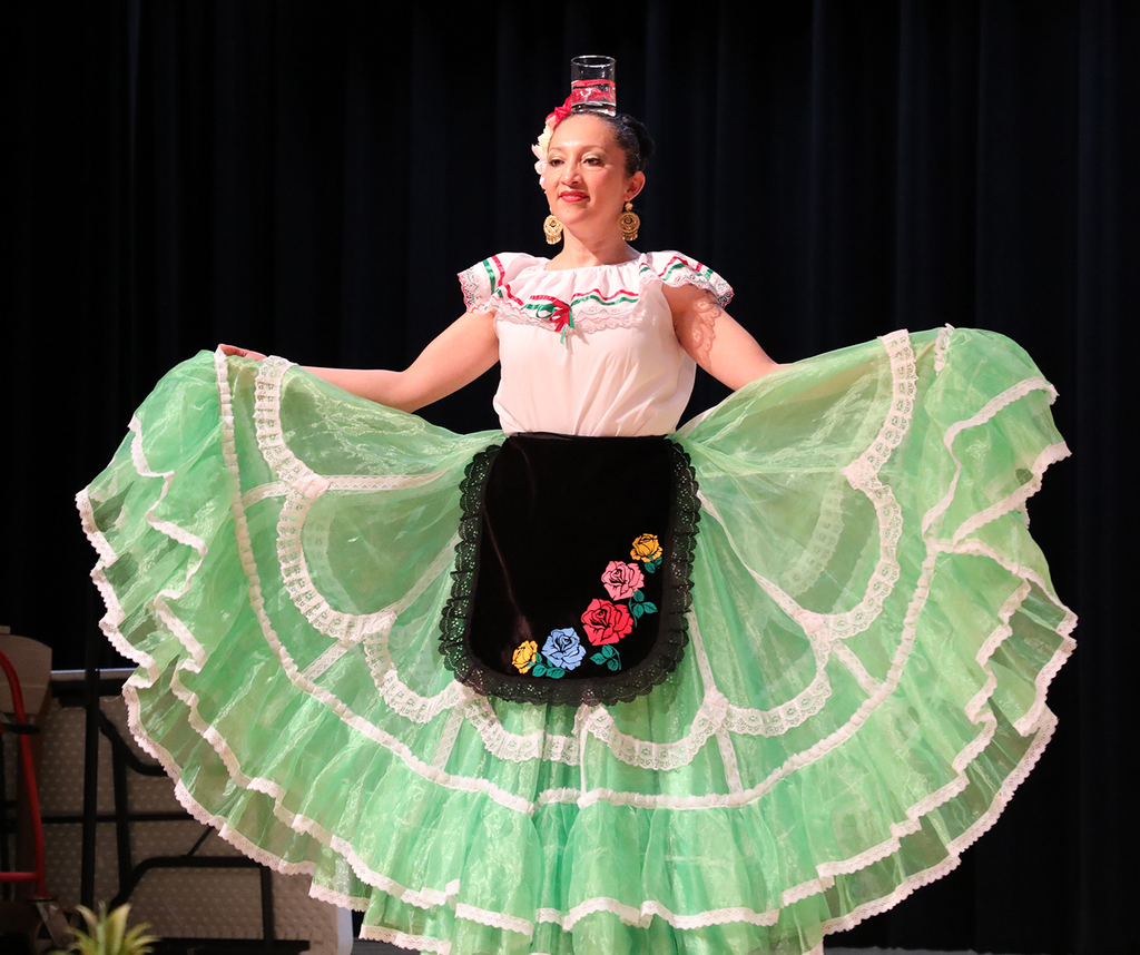A woman in traditional Mexican attire with a glass of water balanced on her head.