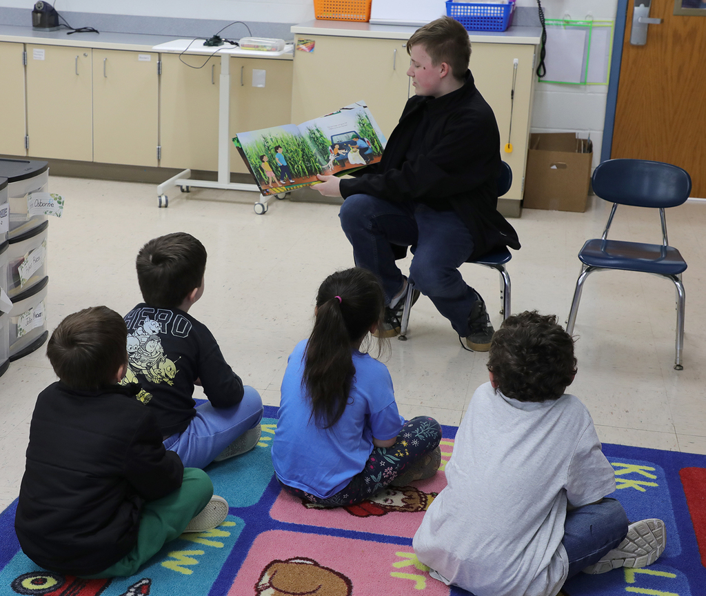 A jr. high student reading to four kindergartners. 