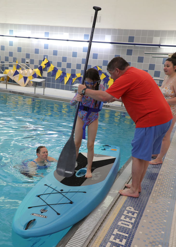 Three adults helping a child on a paddle board in a school swimming pool. 