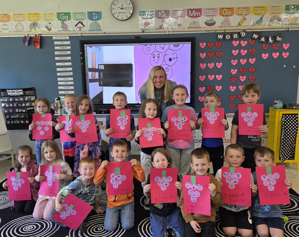 A group of kindergartners holding up artwork. There is one female adult. 