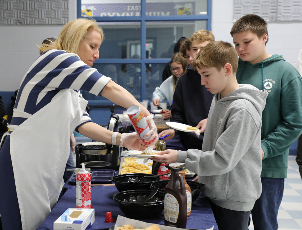 An adult serving students food in a school cafeteria. 