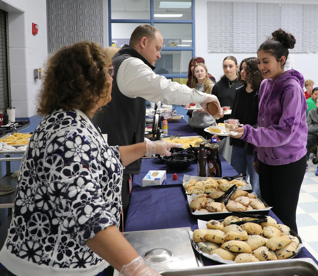 Adults serving students food in a school cafeteria. 