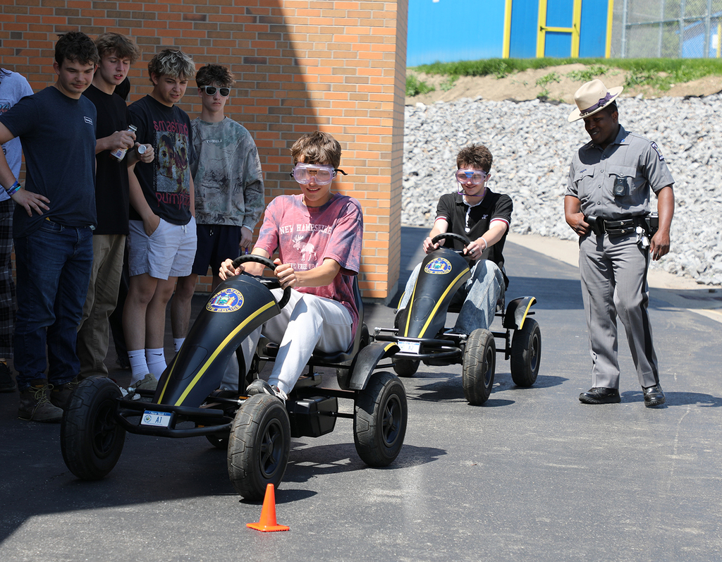 Two boys on peddle cars as a state trooper and other kids look on. 