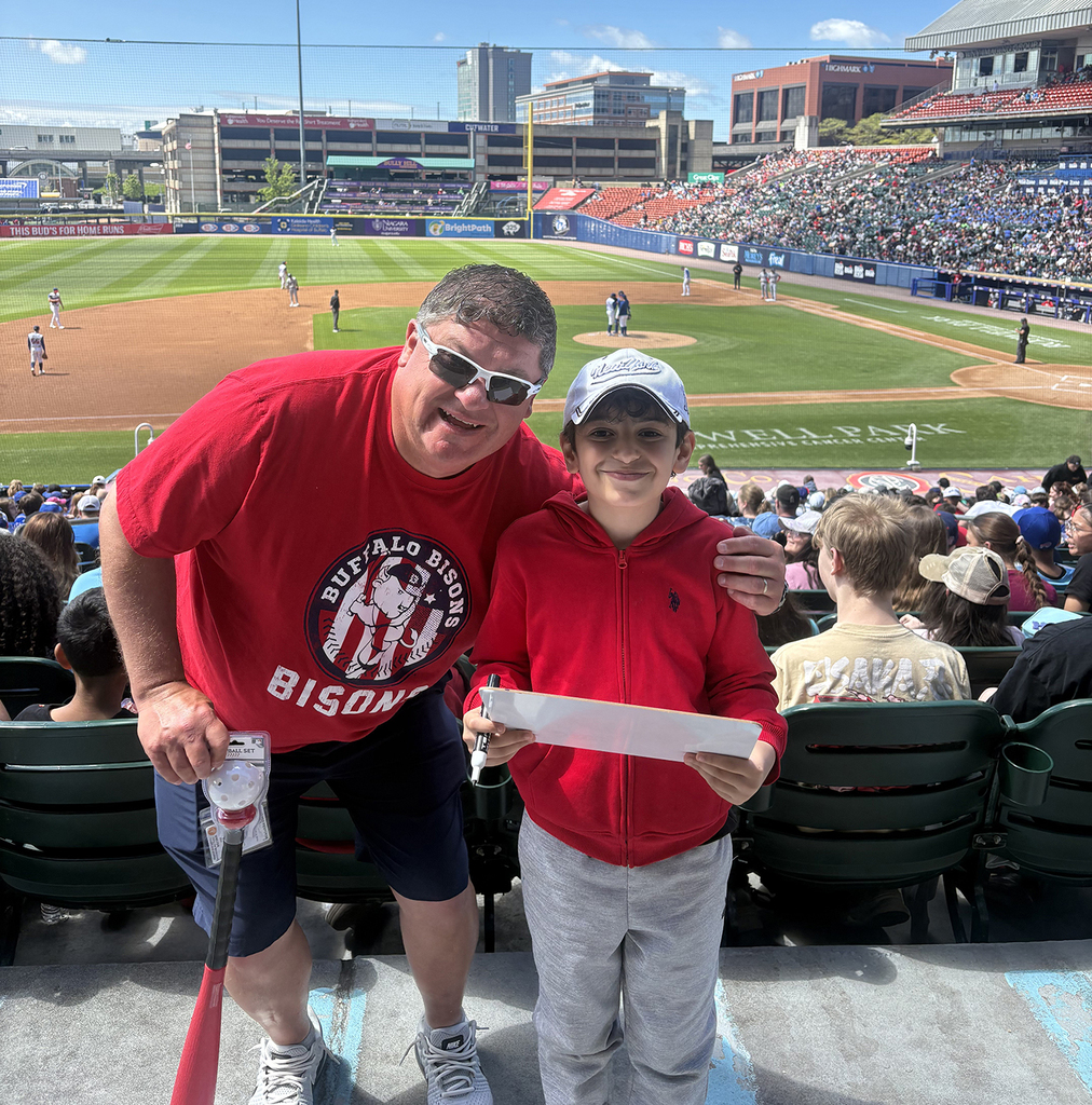 An adult male and a boy standing at a baseball stadium. 