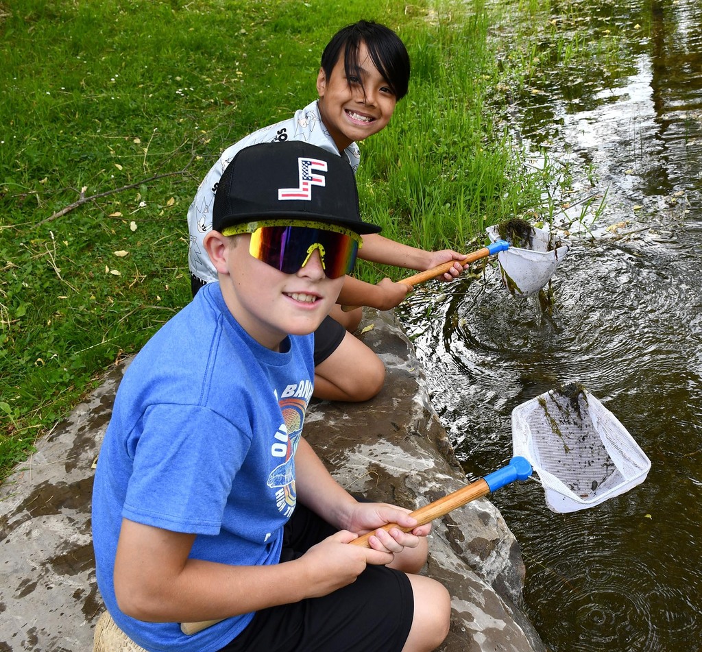 Two boys  sitting by a pond. 