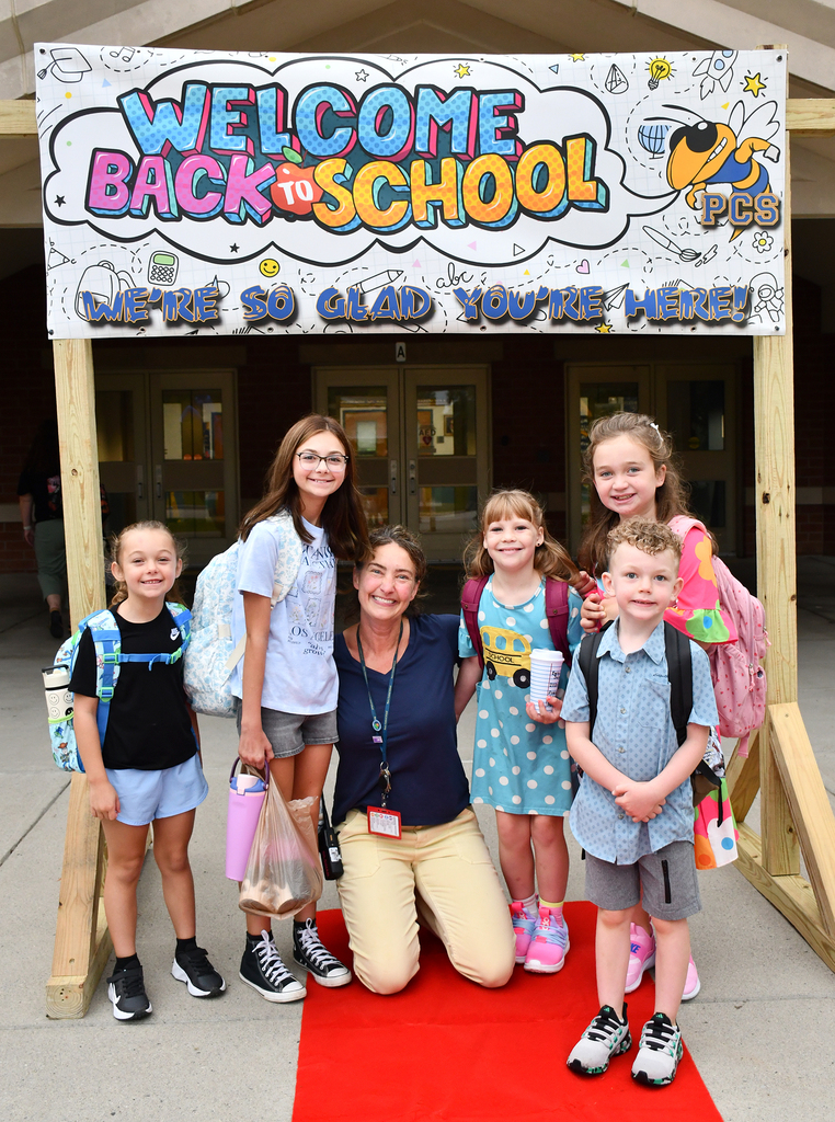 An adult principal posing with several kids. 
