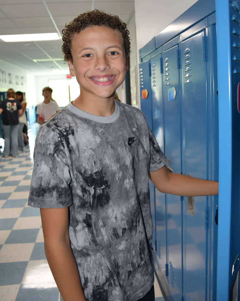 A smiling junior high boy standing at his school locker. 