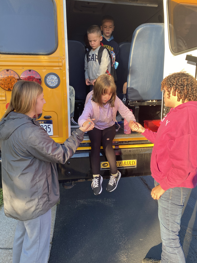 High school students helping younger students off the bus.