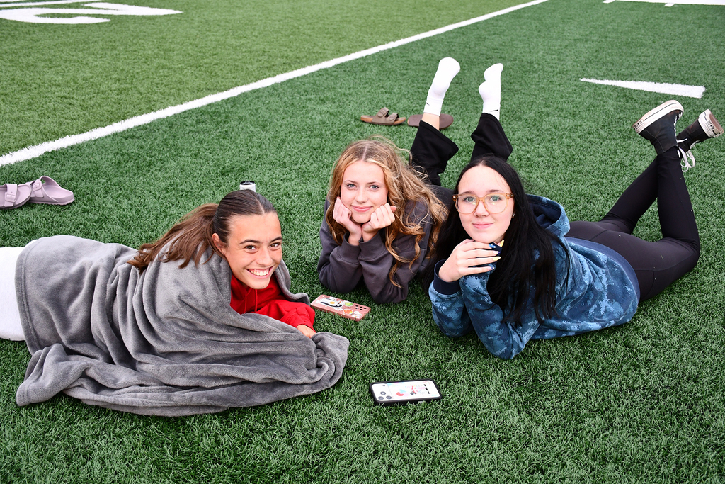 Three seniors laying on a football field. 