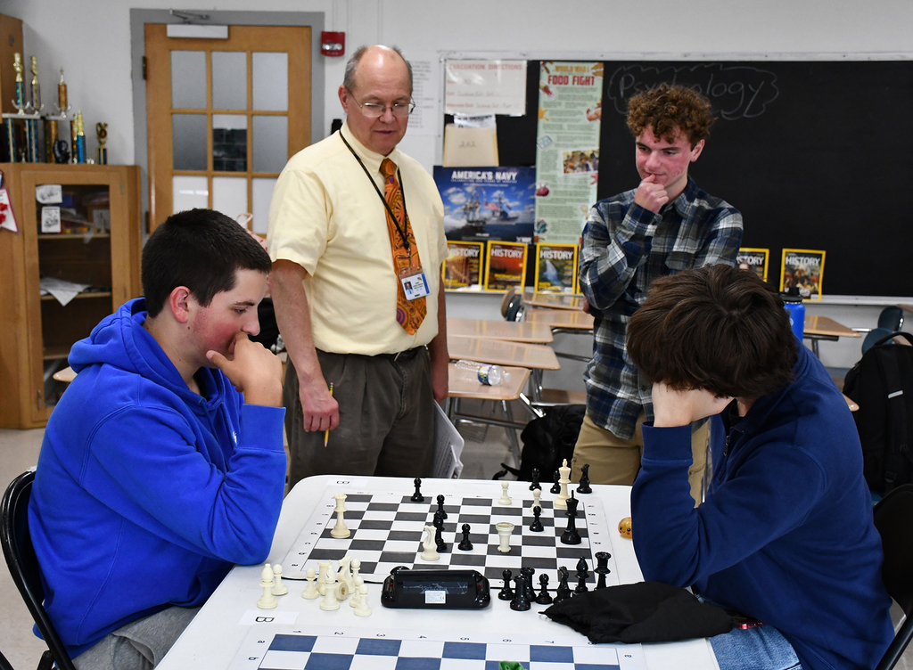Two high school students playing chess, while two others watch. 