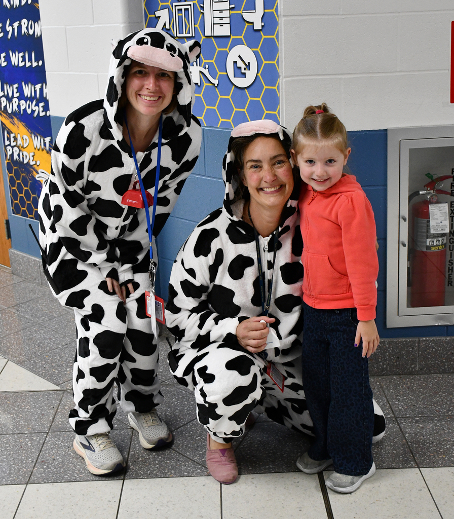 Two adults dressed as cows. They are posing with a child. 
