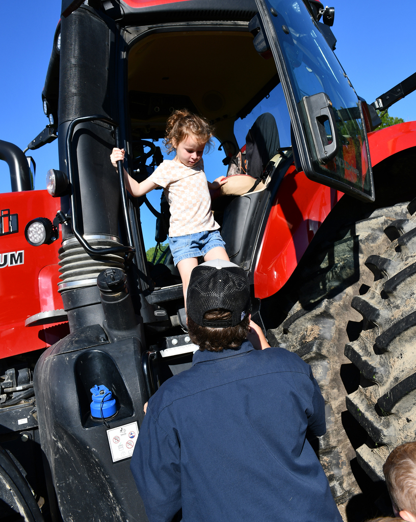 An older student helping a younger student climb down from a tractor. 