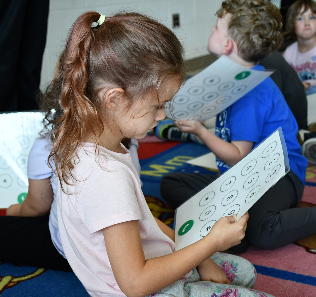 An elementary girl looking at a piece of paper that resembles a phone keypad. 